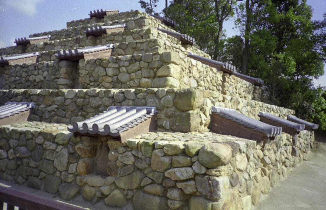 Side view of the Zuto step pyramid's earthen tiers among trees in Takabatake, Nara, Japan